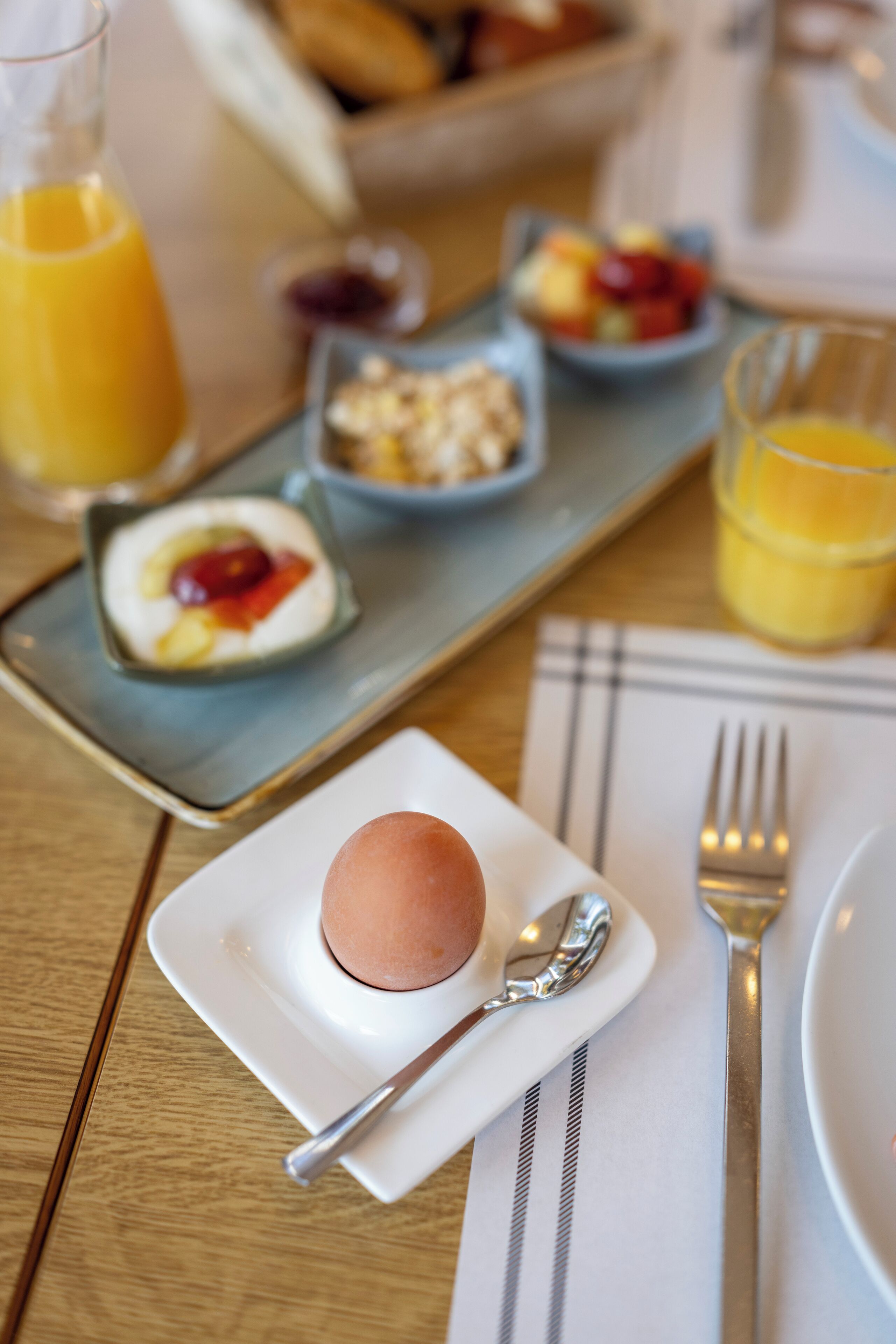 Ein Frühstückstisch mit einem Teller Essen, einem Glas Orangensaft und einer Schale Obst.