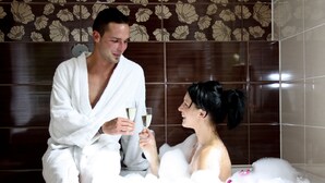 Un couple dans une salle de bain, devant une baignoire remplie de mousse et de pétales de rose.