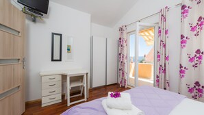 Un dormitorio con cama, escritorio, televisor y puerta corrediza a un balcón.