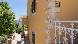 Un estrecho callejón empedrado con un edificio amarillo a la derecha, una reja metálica y vista al mar al fondo.