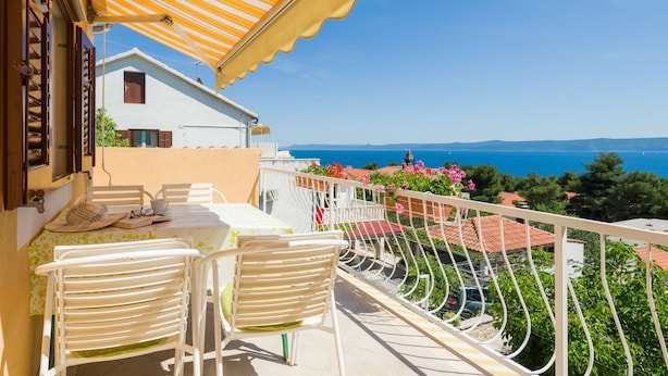 Un balcón con mesa y sillas, con vistas a la costa, casas y un cielo despejado.