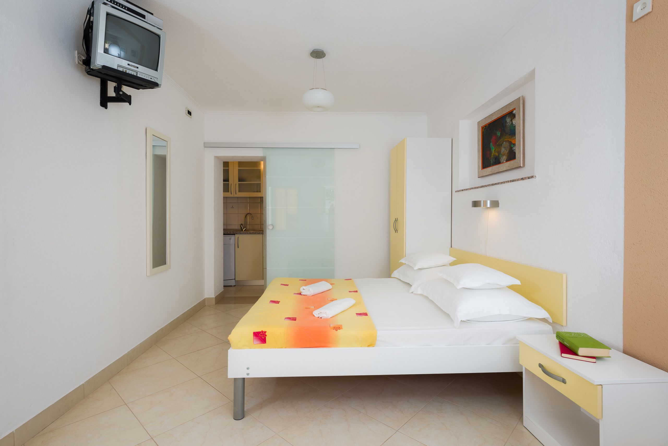 Quarto de hotel com cama, mesa de cabeceira, televisão e banheiro visível por uma porta aberta.