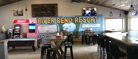Un espace bar avec un plafond en bois, une grande fresque publicitaire pour le River Bend Resort et un téléviseur fixé au mur.