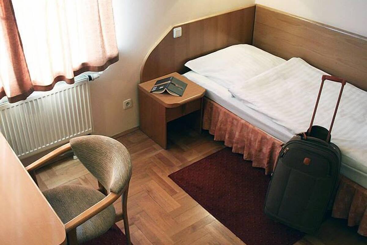 A compact hotel room with a single bed, a small desk, a chair, and a suitcase.
