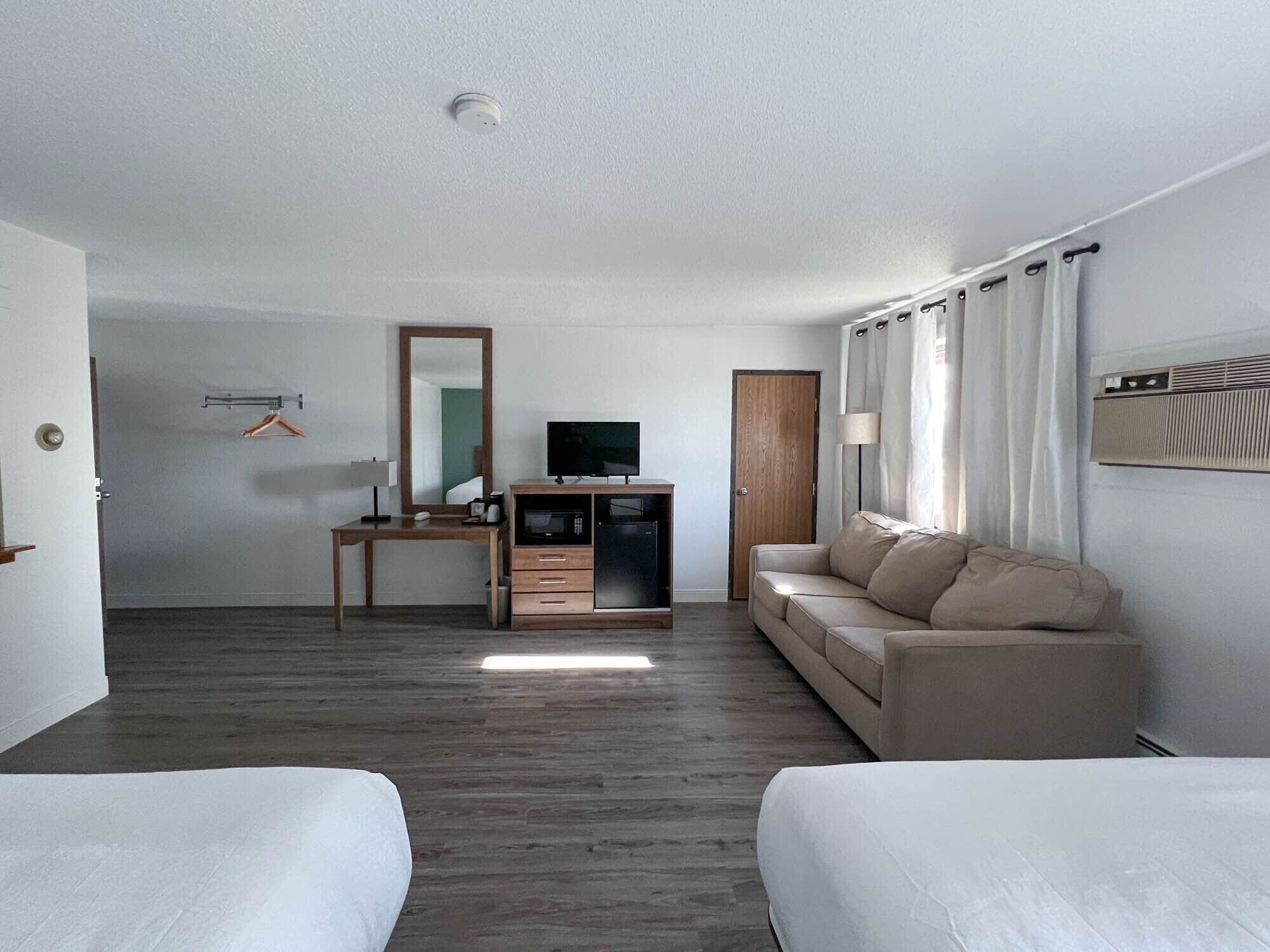Ett hotellrum med ett skrivbord i trä, en tv, en soffa och en säng.