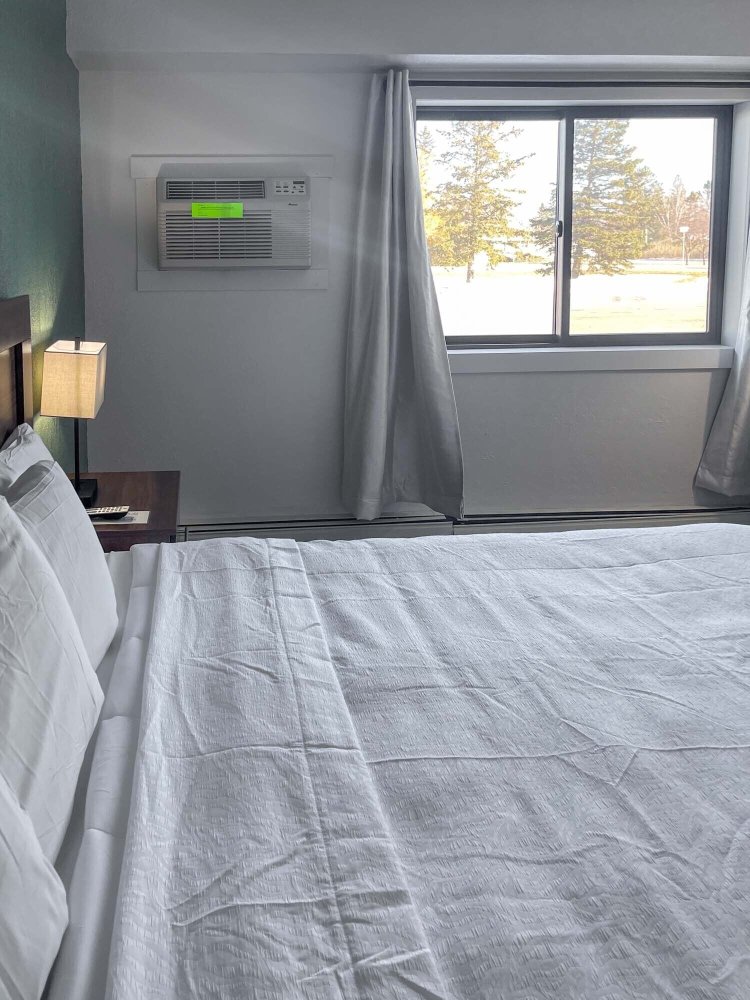 Una habitación de hotel con cama, aire acondicionado, lámpara y ventana con cortinas.