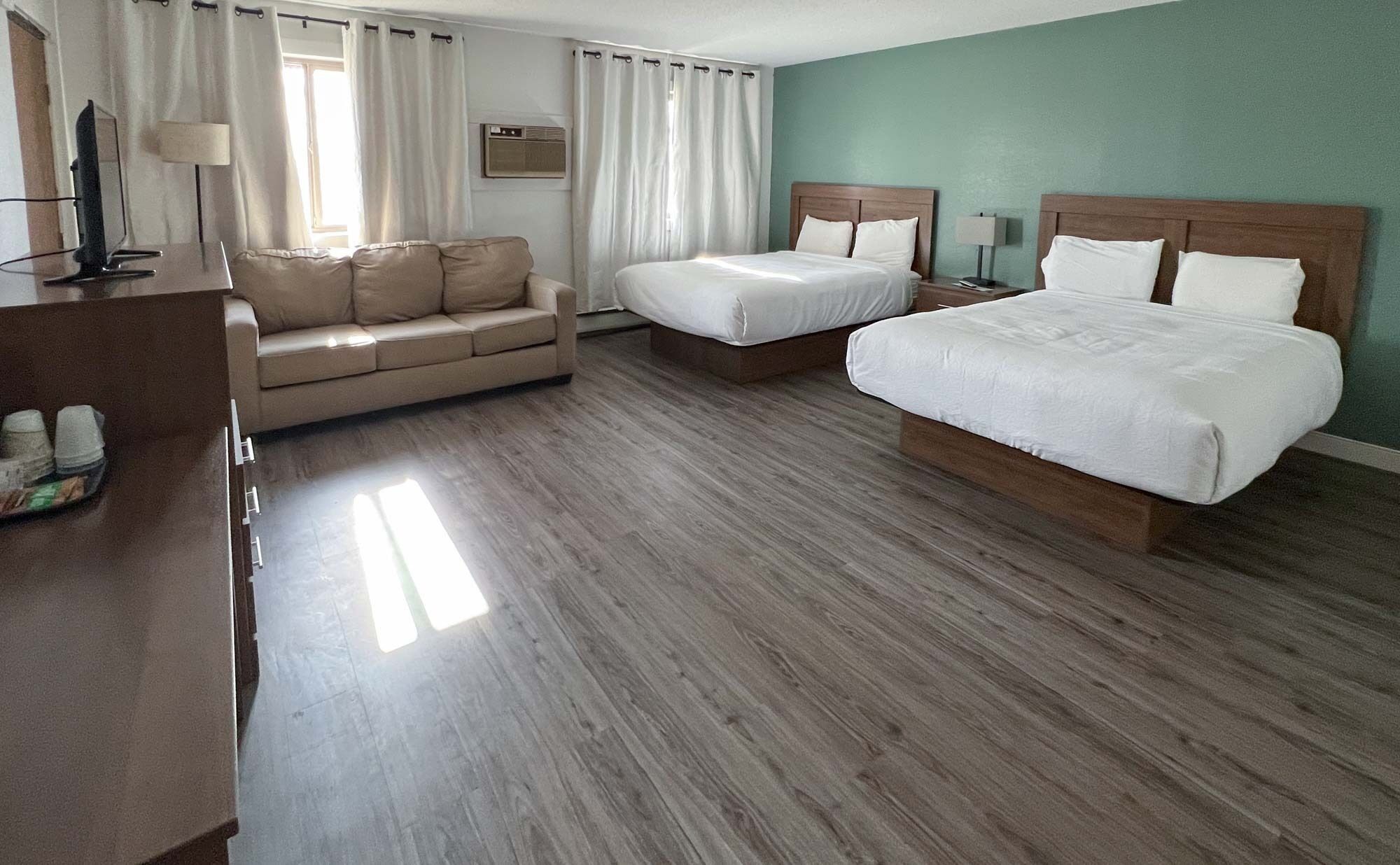 Una habitación de hotel con piso de madera, dos camas, un sofá, un televisor y una lámpara.