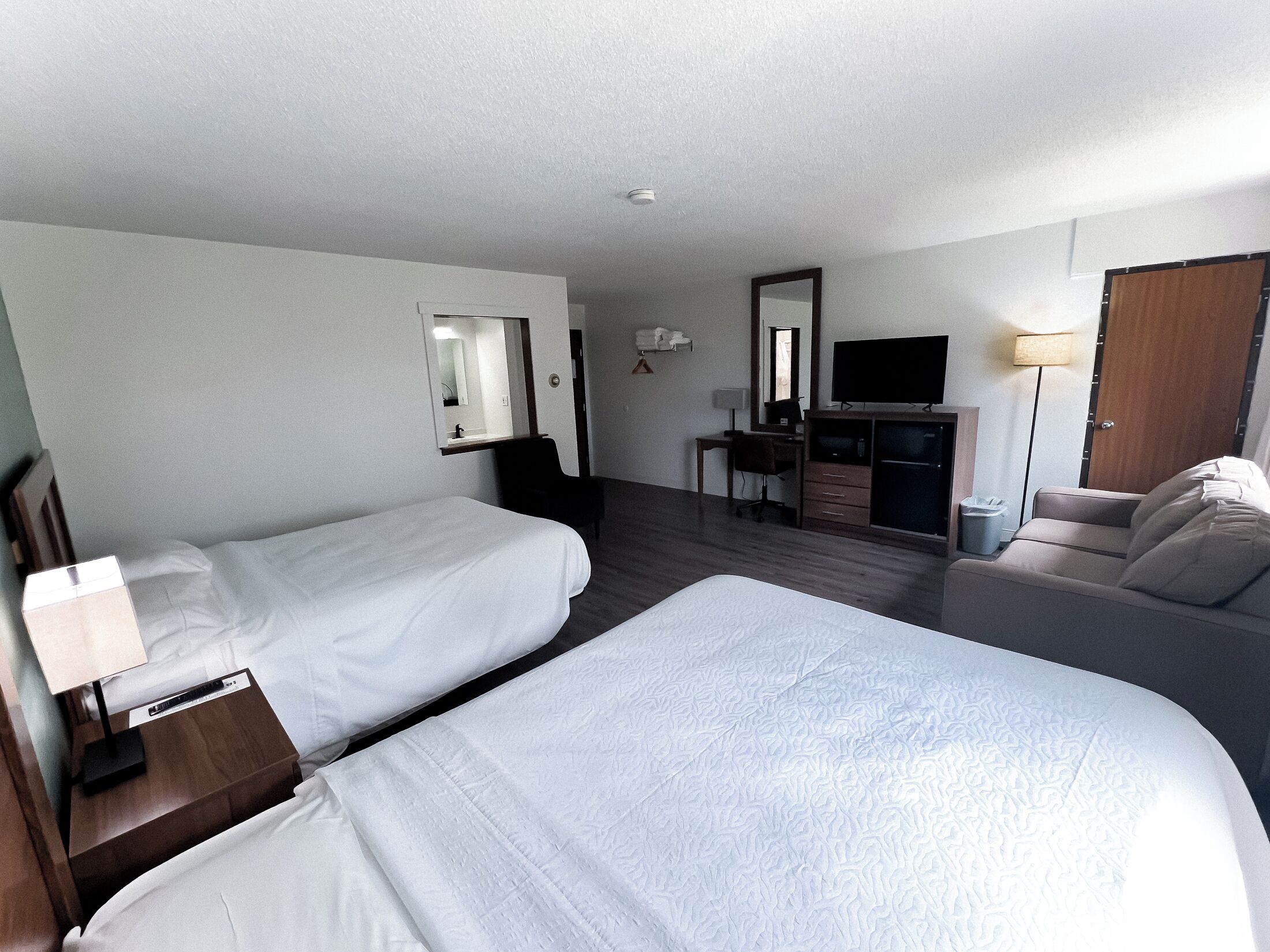 Una habitación de hotel con dos camas, un escritorio con silla, un televisor y un sofá.