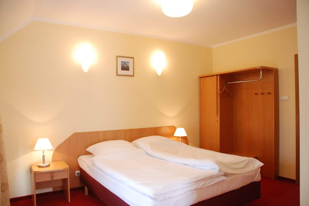Habitación de hotel con una cama de madera, dos lámparas de noche, un armario de madera y un cuadro enmarcado en la pared.