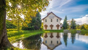 A hotel with a reflection in a pond, surrounded by greenery and trees. - Hotel Karczyce (gmina Kostomloty)