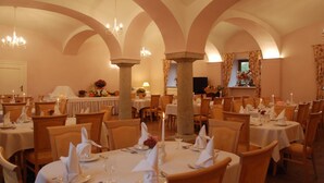 A restaurant with multiple tables, each set with white tablecloths, candles, and napkins. The room features arched ceilings and chandeliers. - Hotel Karczyce (gmina Kostomloty)