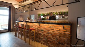 A bar area with a brick wall, wooden chairs, and a counter with bottles. - Hotel Karczyce (gmina Kostomloty)