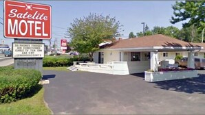 A Satellite Motel with a signboard, a covered parking area, and a small building with a sloped roof. - Satelite Motel (Sault Ste. Marie)