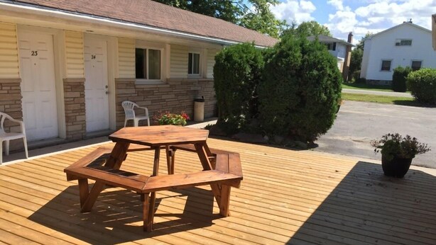 A wooden deck with a picnic table, a small garden with a potted plant, and a row of numbered doors on a building. - Satelite Motel (Sault Ste. Marie)