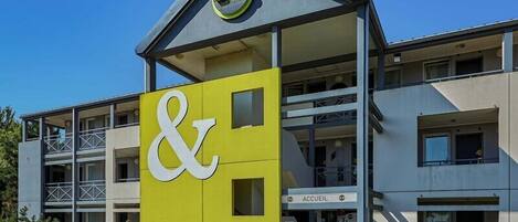 A B&B building with a prominent yellow and white sign, a balcony, and a clear sky.