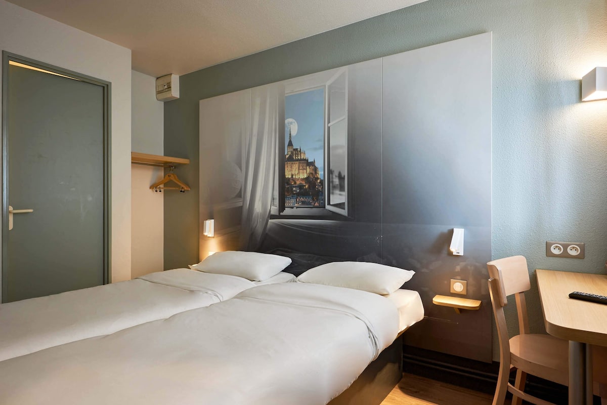 Habitación de hotel con cama, escritorio y silla. En la pared, un cuadro que muestra un paisaje urbano.