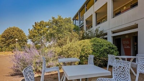 Outdoor seating with white chairs and tables, a building with balconies, and a clear sky.