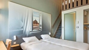 A hotel room with a bed, a desk, a chair, a staircase, and a door.