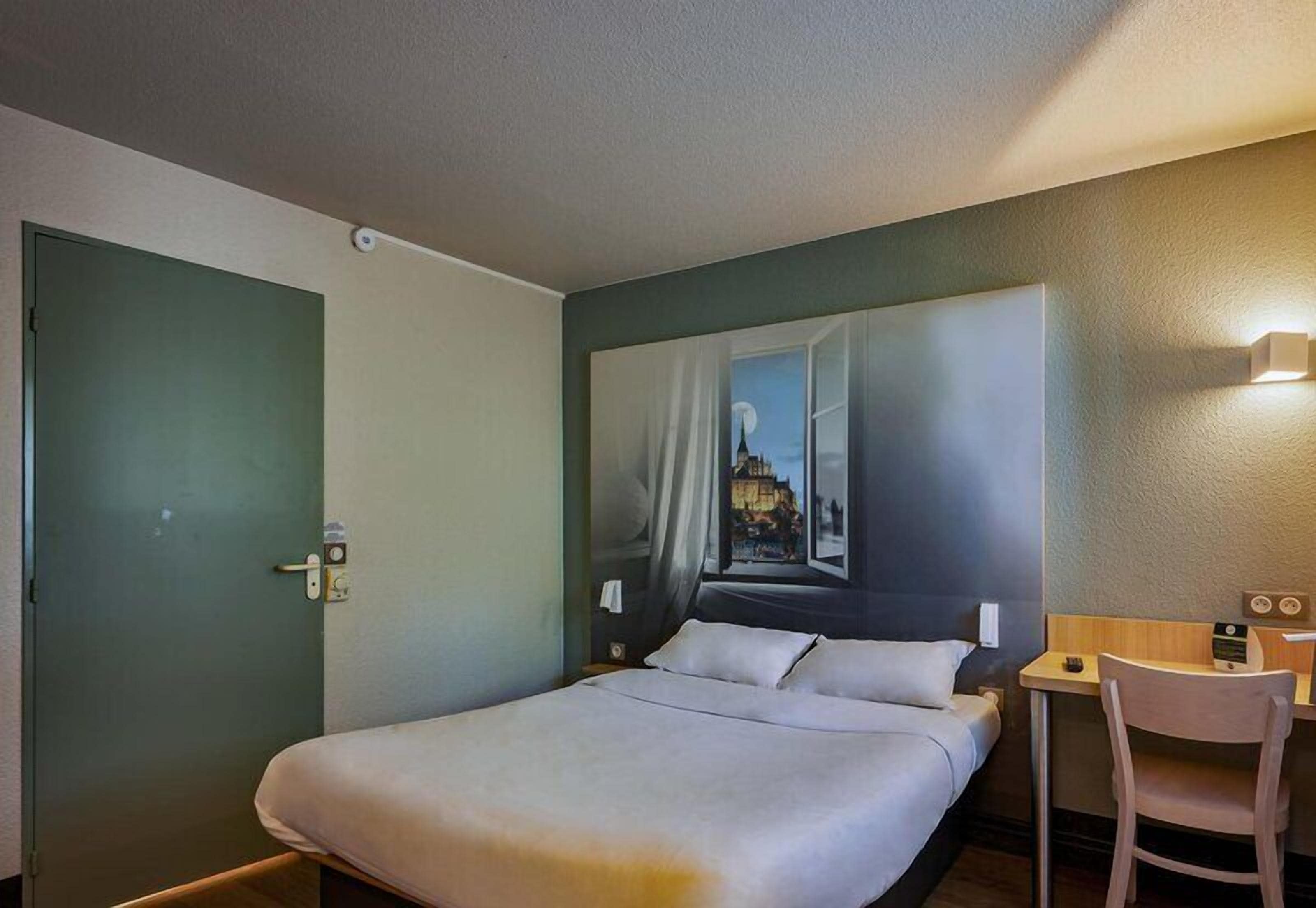 Hotellihuone, jossa on sänky, työpöytä, tuoli ja taulu seinällä.
