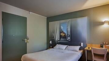 A hotel room with a bed, a desk, and a chair.