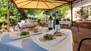 Un espace de restauration en plein air avec des tables protégées par des parasols jaunes, où l’on peut voir des assiettes remplies de nourriture et des bouteilles de vin.