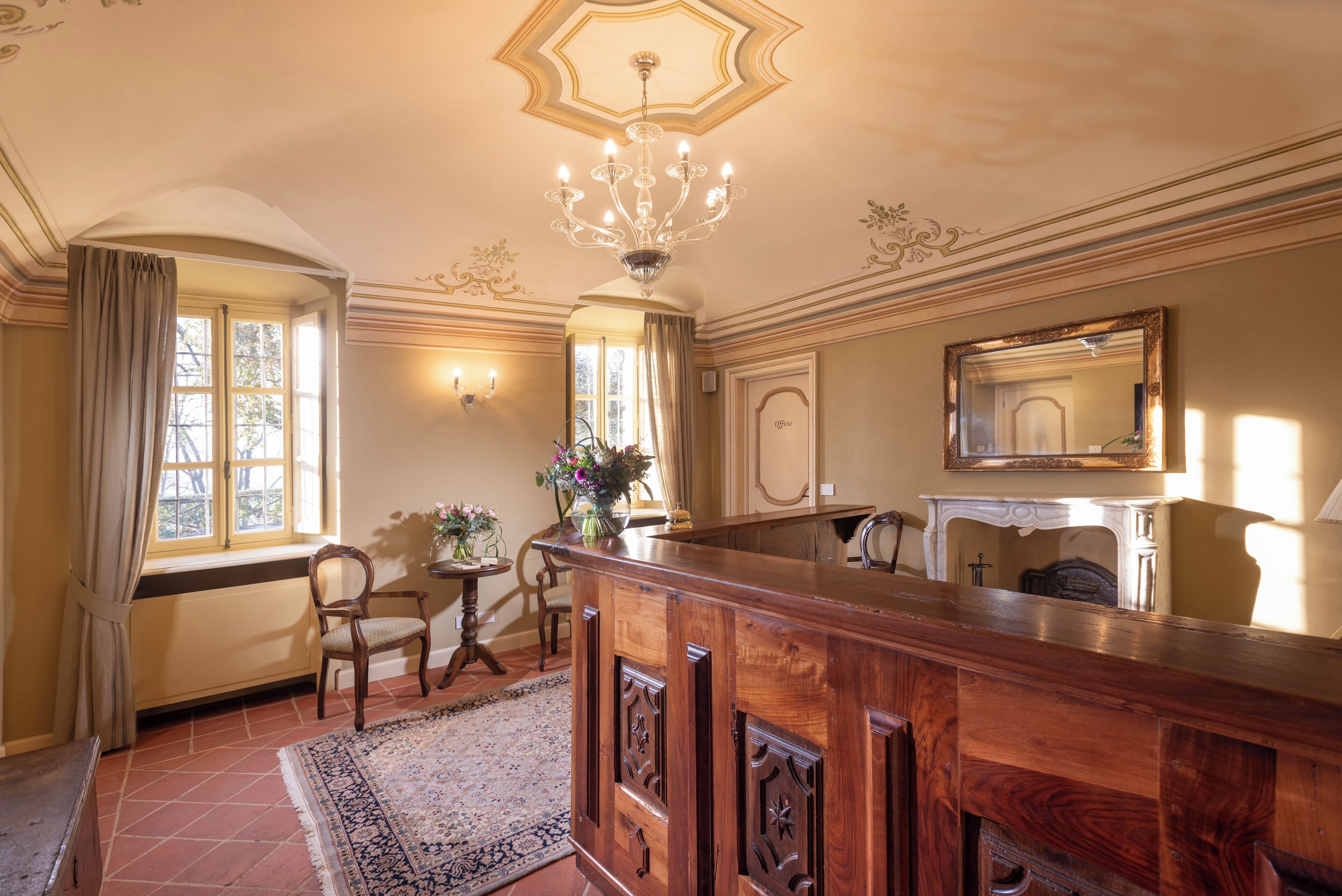 Un'ampia stanza con un'elegante vetrina in legno, un lampadario, un camino e un grande specchio.