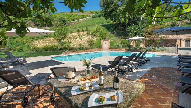 Un espace aménagé au bord de la piscine, avec des chaises longues, une table à manger dressée avec des assiettes de nourriture et une bouteille de vin.