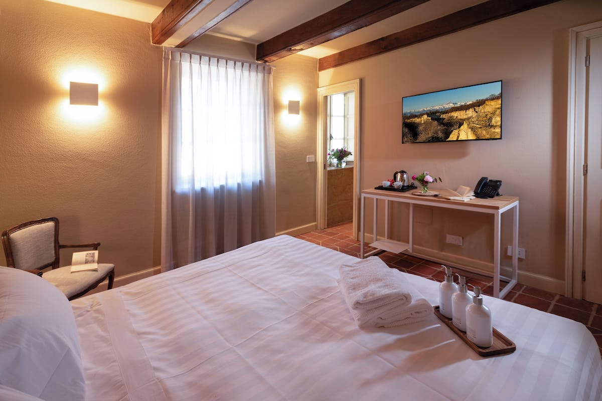 Habitación de hotel con cama, escritorio con artículos de aseo, silla y un cuadro en la pared.