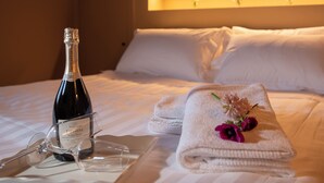 Un lit parfaitement fait, avec une bouteille de champagne, des verres et une serviette décorée de fleurs.