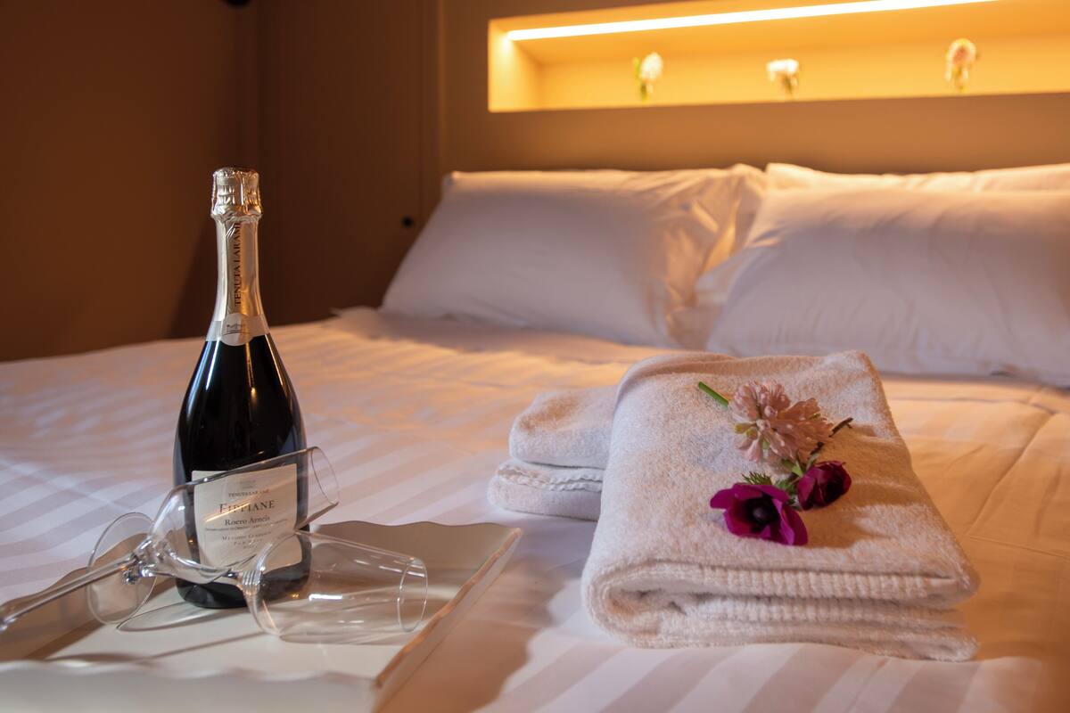 Una cama impecable con una botella de champán, copas y una toalla con flores.