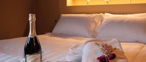 A neatly made bed with a bottle of champagne, glasses, and a towel with flowers.