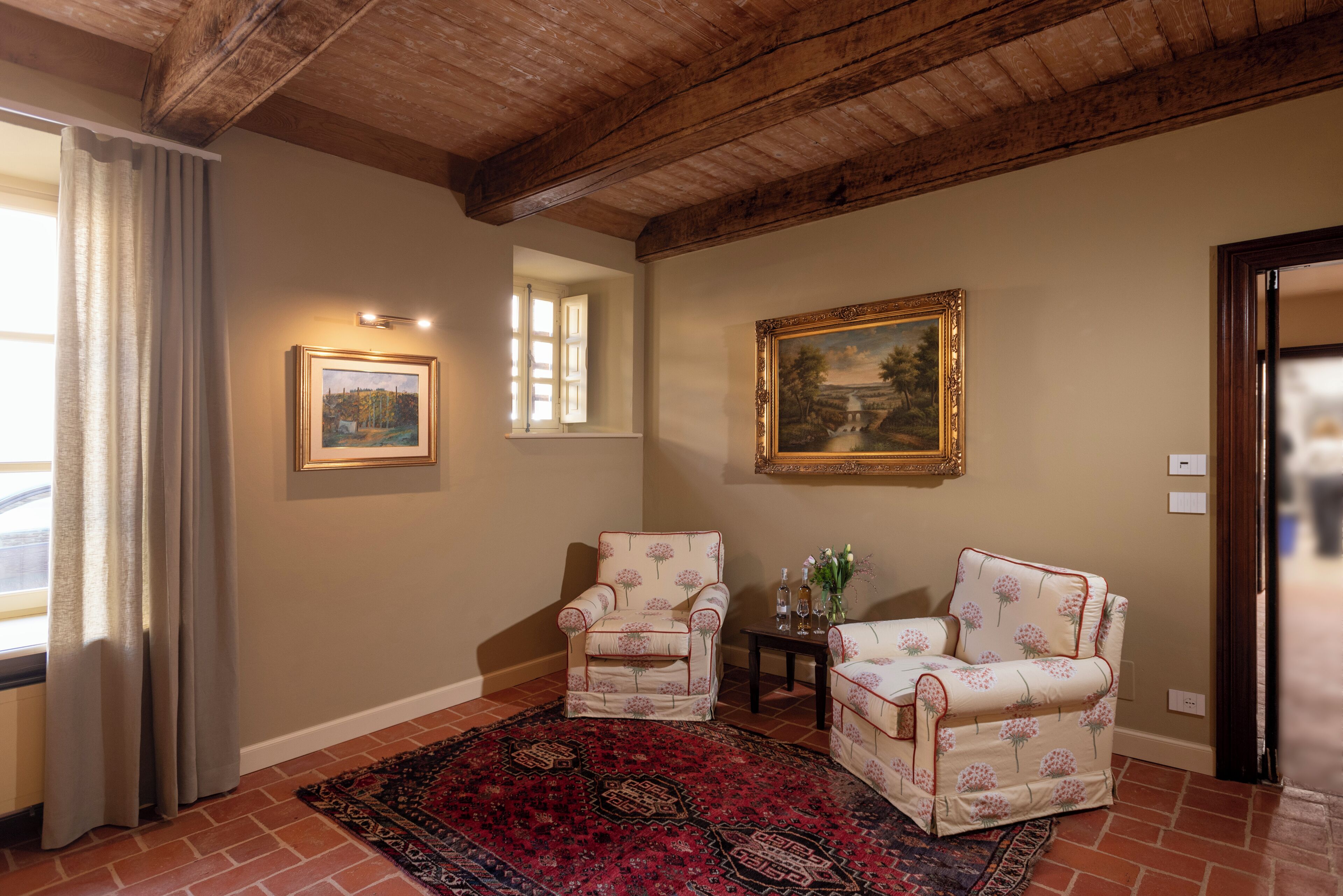 A room with two armchairs, a patterned rug, and two framed paintings on the wall.