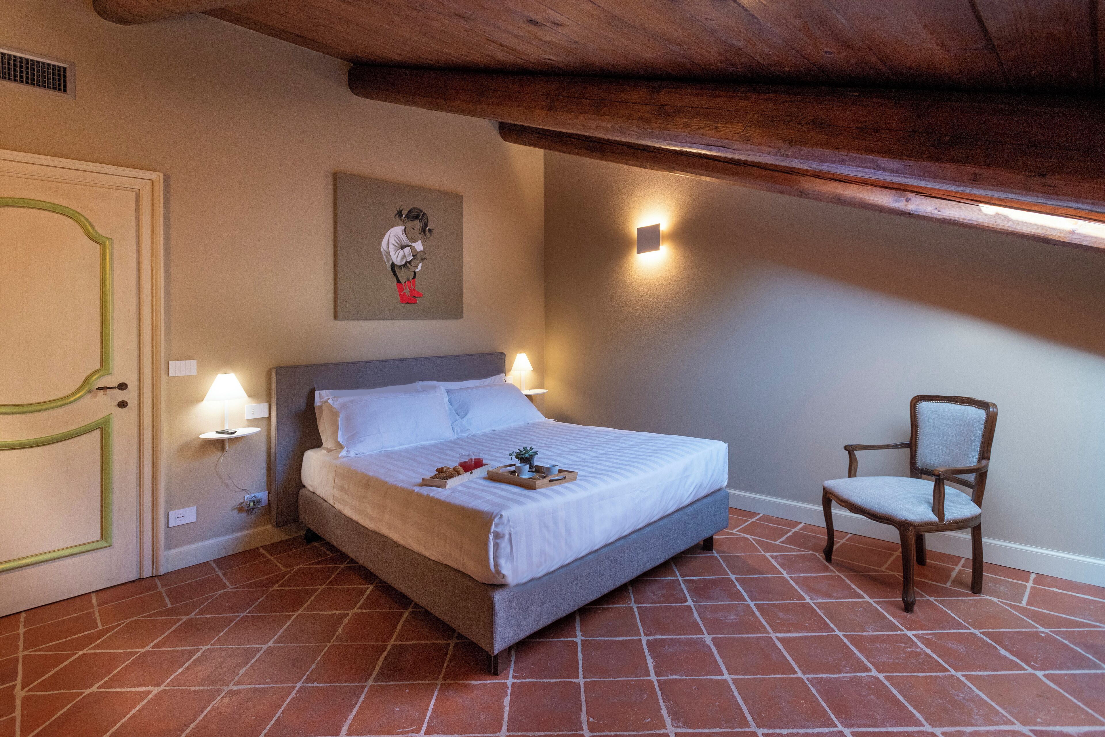 A bedroom with a bed, a chair, a wall-mounted picture, and a light fixture.