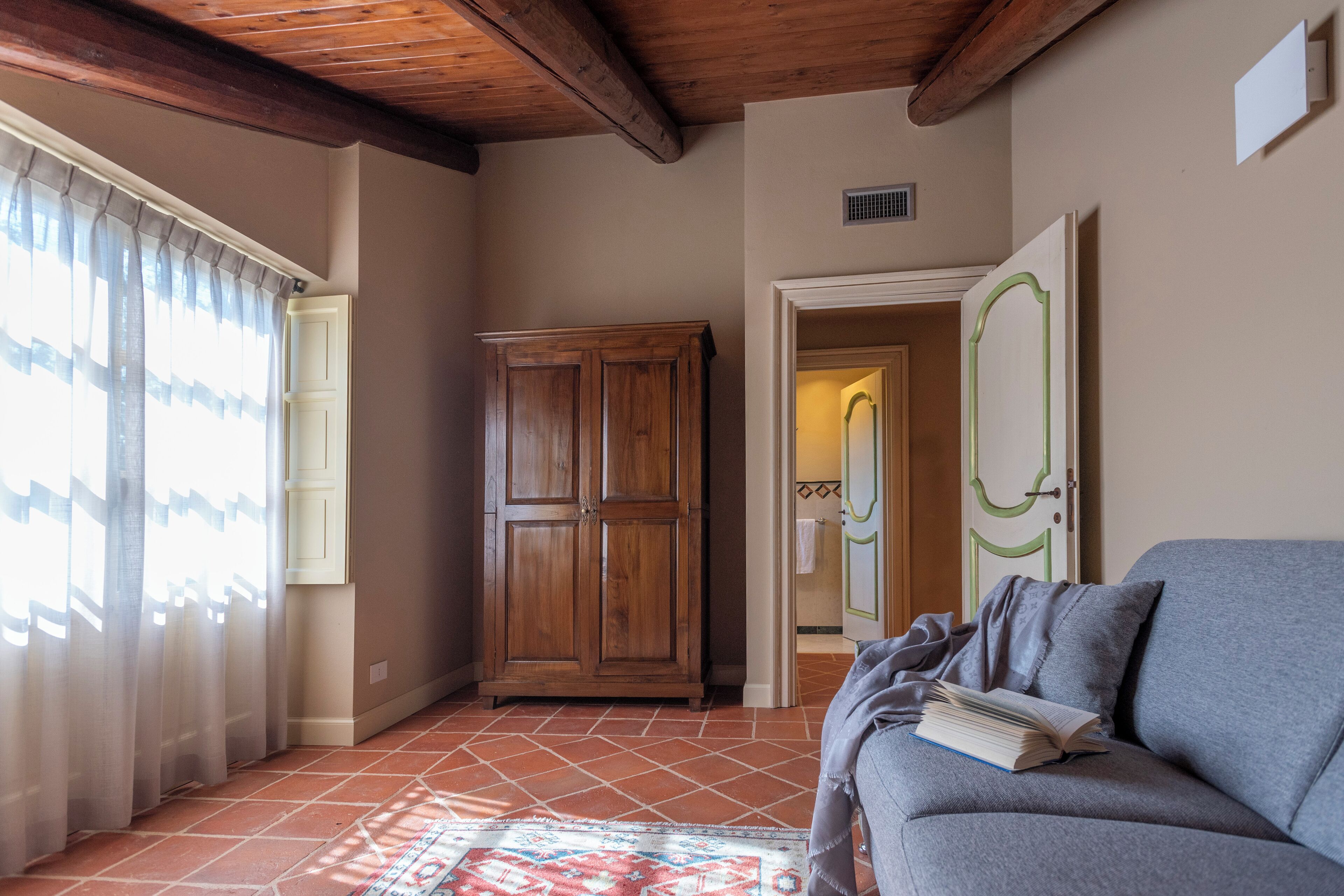 A room with a sofa, a wooden wardrobe, a patterned rug, and a door leading to a bathroom.