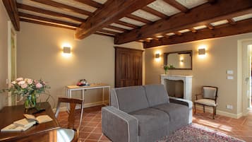 Ein Wohnzimmer mit grauem Sofa, Holzbalkendecke, Kamin und Essbereich mit Tisch und Stühlen.