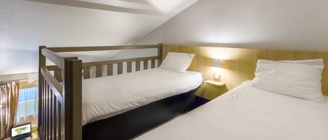A room with a bunk bed, a desk with a laptop, and a bedside table with a lamp.