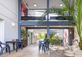 Un espace extérieur abrité, avec des tables et des chaises, une statue et une vue sur la rue.