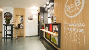 A reception area with a wooden reception desk, a clock, and a welcome sign. - B&B HOTEL Rennes Sud Chantepie (Rennes)