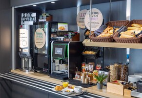 Un buffet de petit-déjeuner comprenant des machines à café, du pain, des viennoiseries et diverses garnitures.