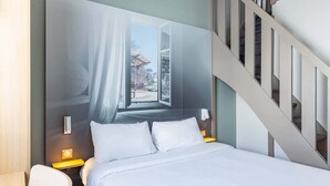A modern hotel room with a large bed, a nightstand, a chair, and a staircase. - B&B HOTEL Rennes Sud Chantepie (Rennes)
