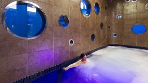 Une personne se trouve dans une grande piscine intérieure, dont les murs sont dotés de nombreuses fenêtres circulaires.