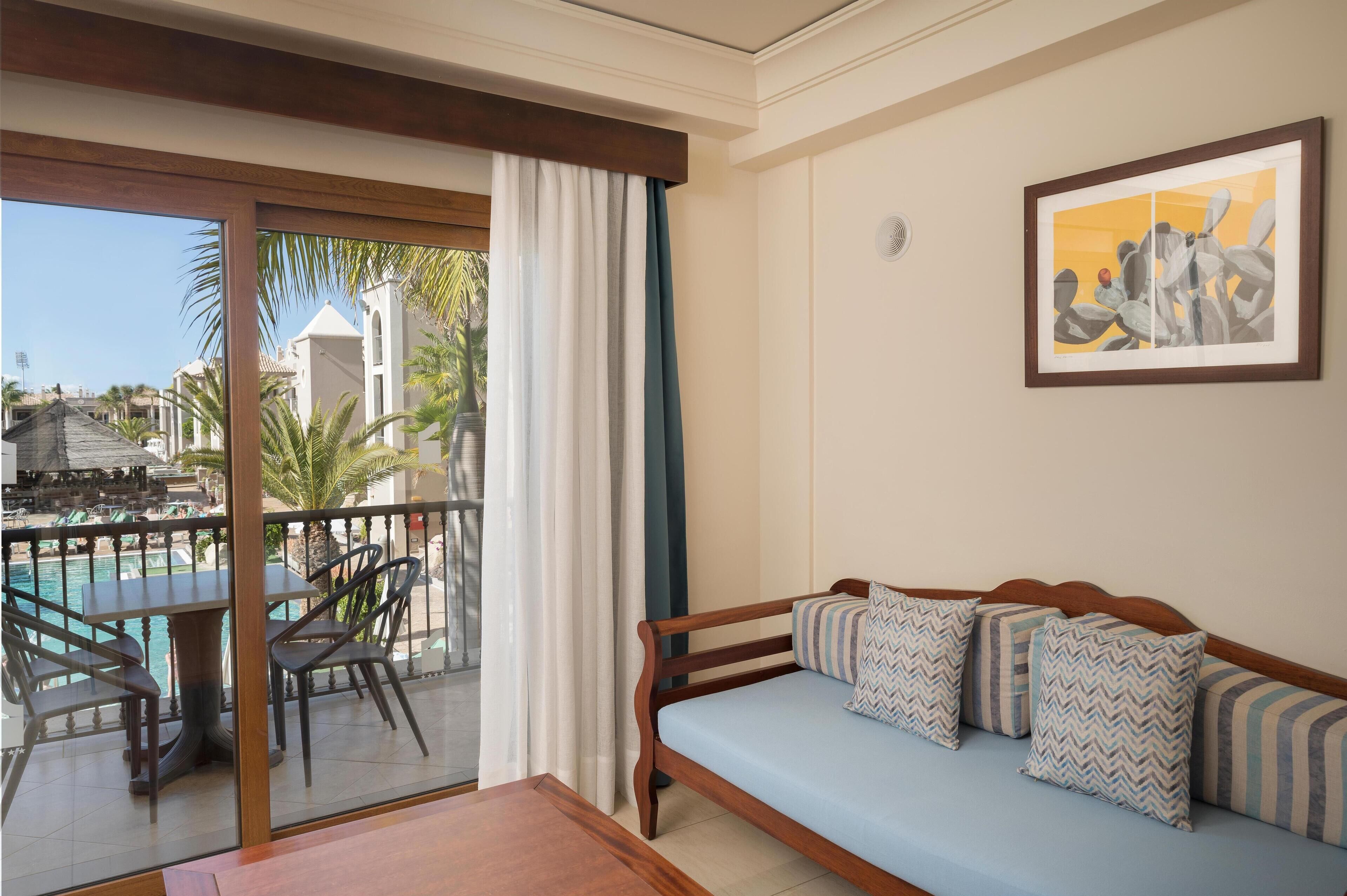 A hotel room with a balcony, a sofa, a table, and chairs.
