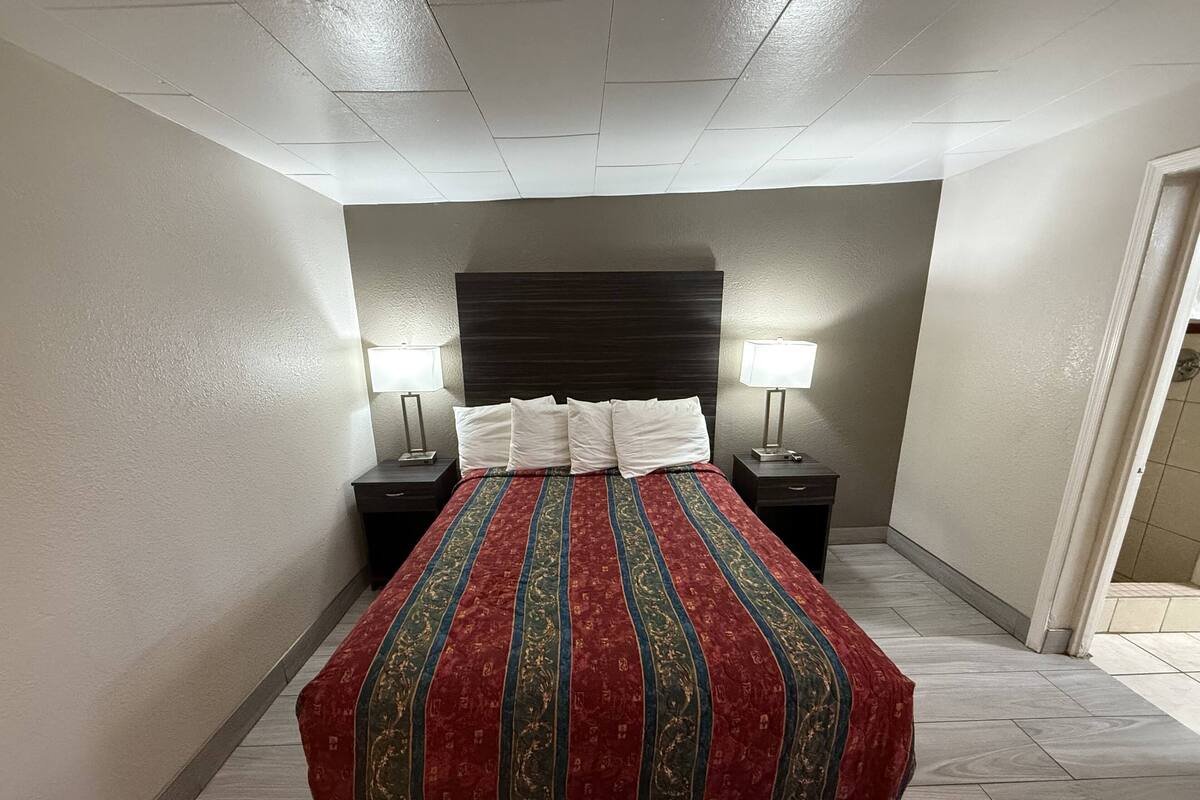 A hotel room with a large bed, two bedside tables with lamps, and a dark headboard.