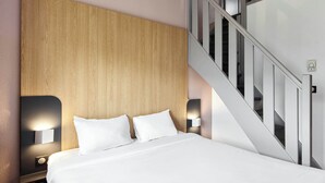 Een moderne hotelkamer met een houten hoofdeinde, een bed met witte lakens, twee bedlampjes en een trap met glazen balustrades.