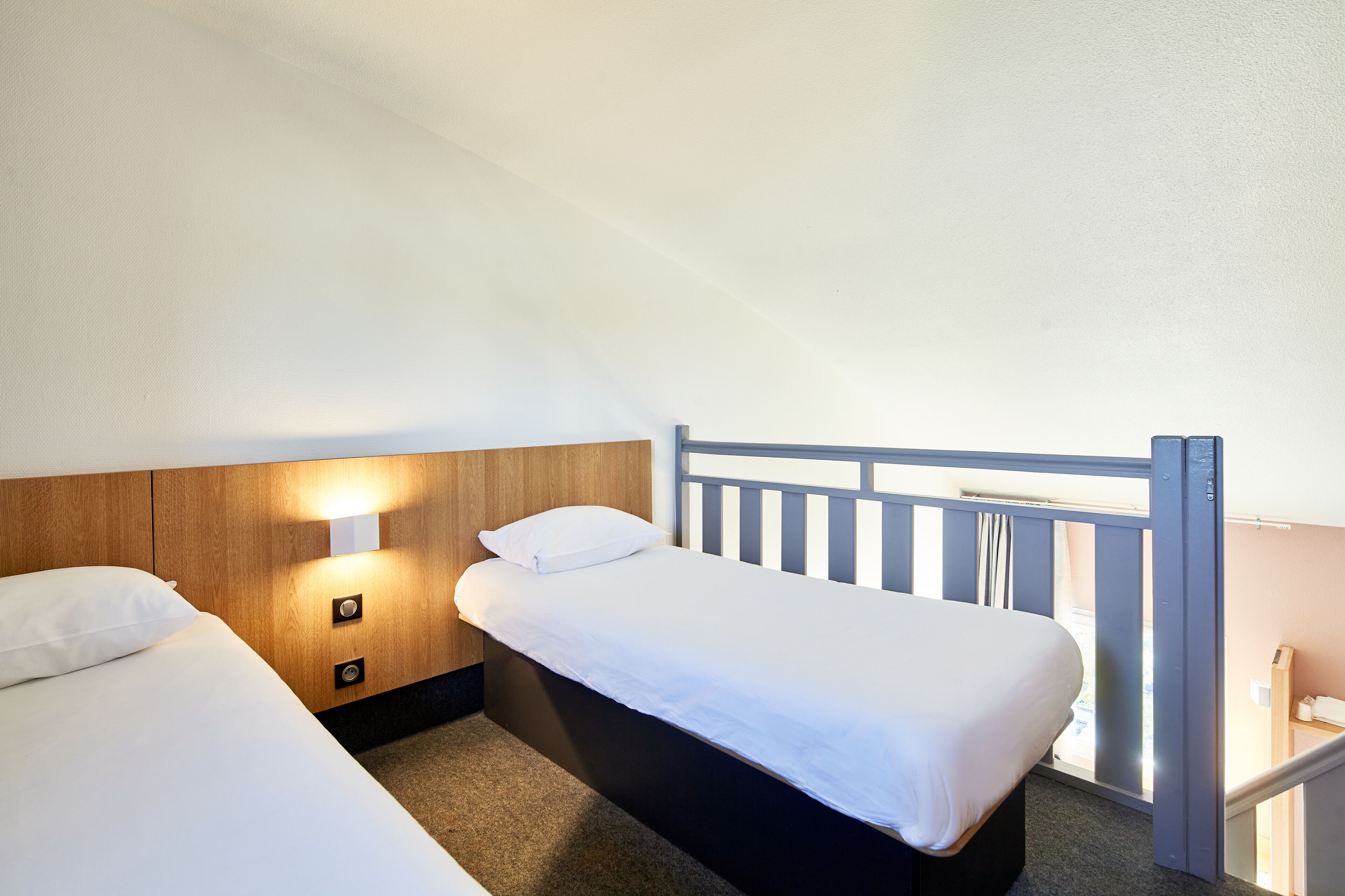 A bedroom with two beds, a wooden headboard, and a nightstand with a lamp.