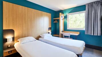Habitación de hotel con dos camas, un escritorio, una silla, perchero y ventana con cortinas.