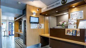 A reception area with a wooden reception desk, a monitor displaying information, and a sign that reads "Bienvenue chez B&B Hotels." - B&B HOTEL Périgueux Boulazac (Boulazac-Isle-Manoire)