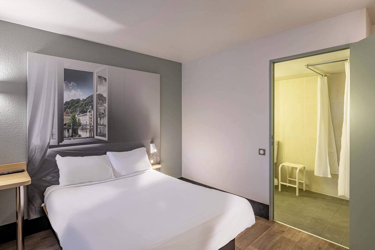 A modern hotel room with a large bed, a nightstand, a painting, and a view of the bathroom.