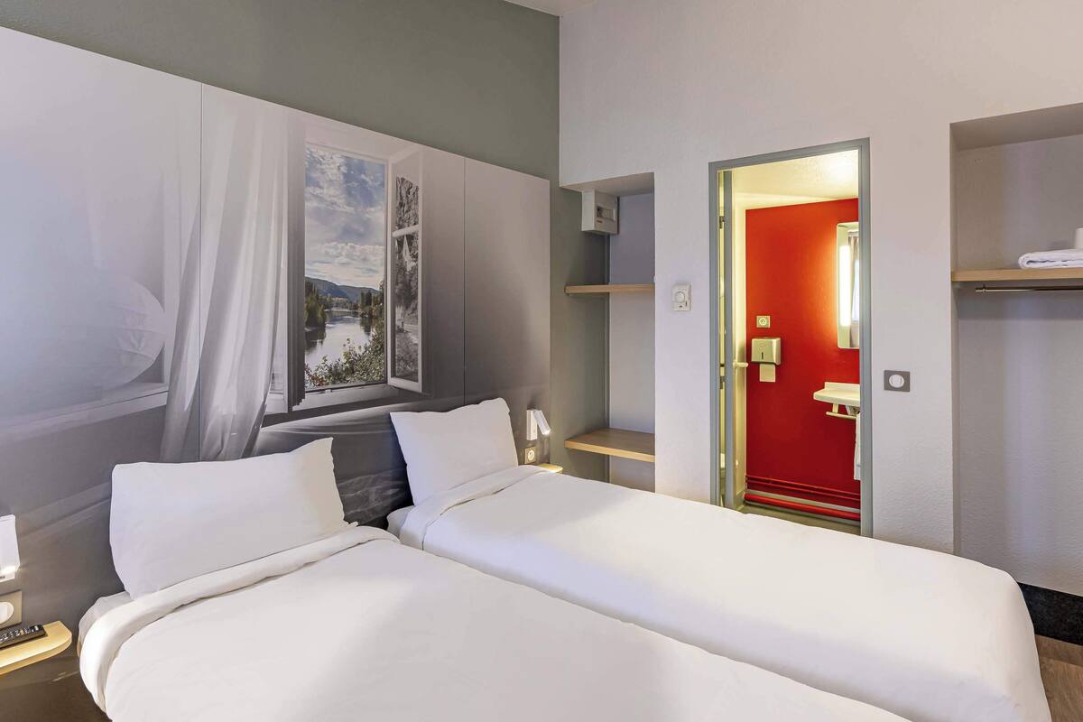 A hotel room with a bed, a nightstand, a wall-mounted shelf, and a door leading to a bathroom.