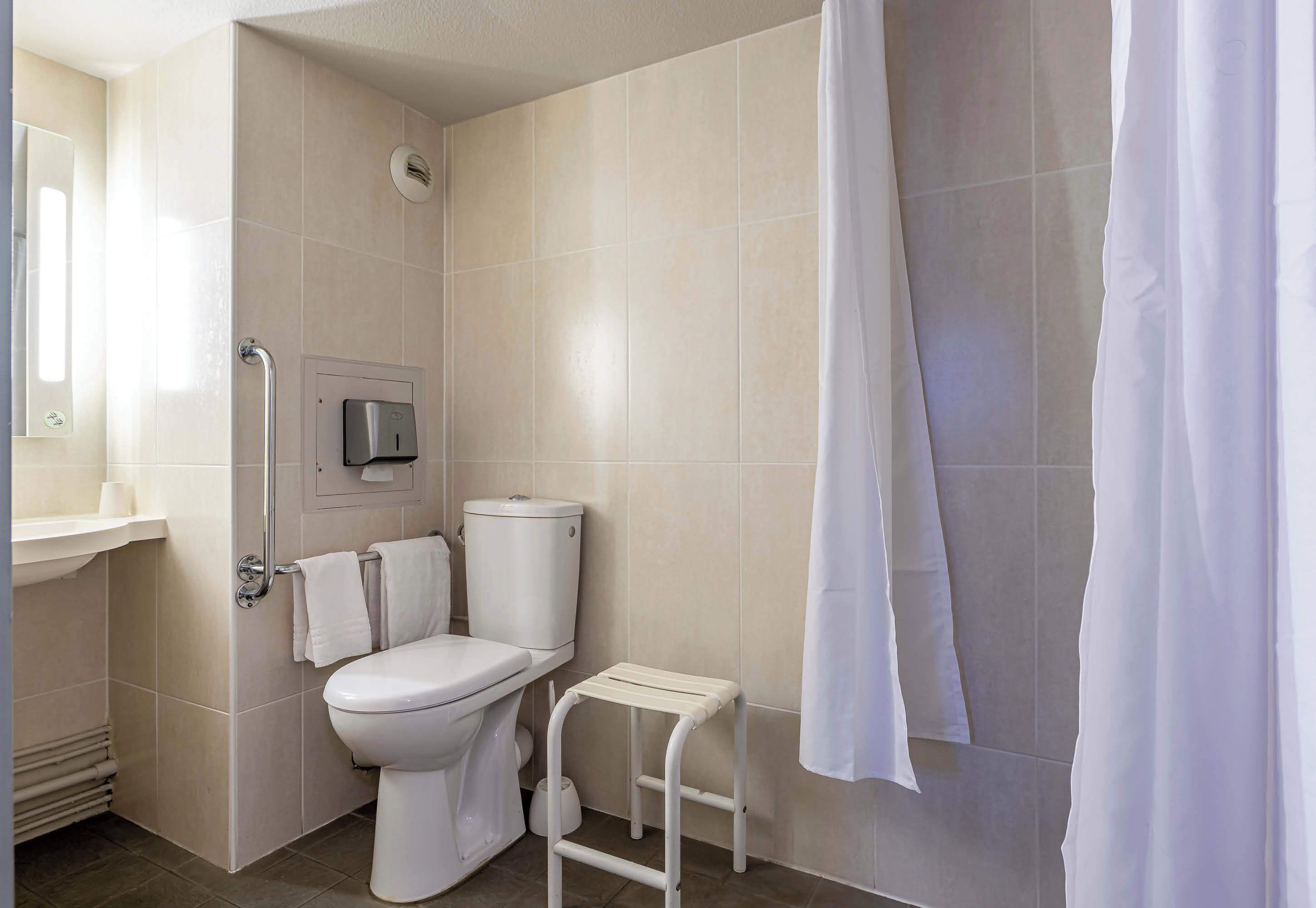 A modern bathroom with a toilet, a small step stool, a hand dryer, and a shower curtain.